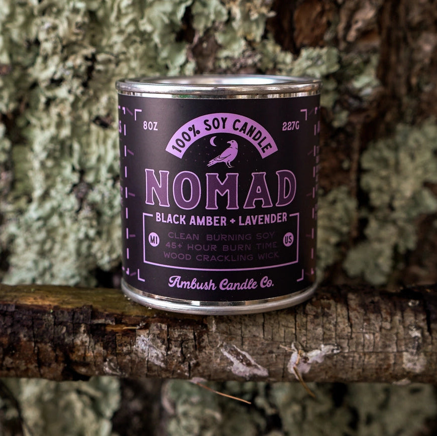 Candle canister labeled 'Nomad' on a tree branch
